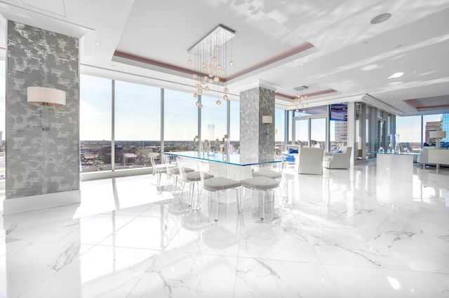 interior space with a raised ceiling, a wall of windows, a chandelier, and light tile floors