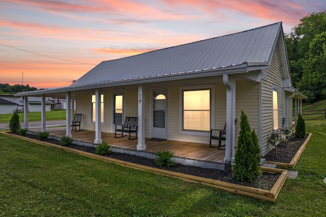 back house at dusk with covered porch and a lawn