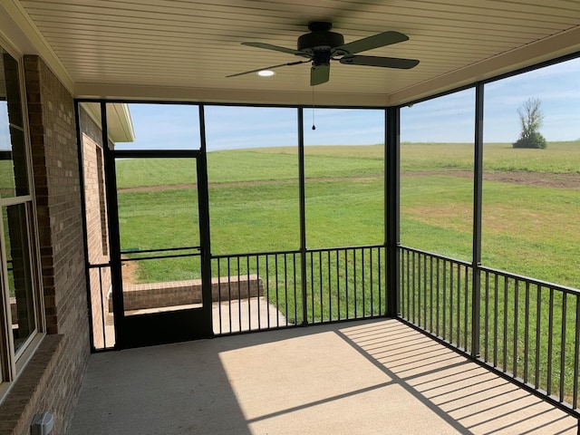 unfurnished sunroom with ceiling fan, wood ceiling, plenty of natural light, and a rural view