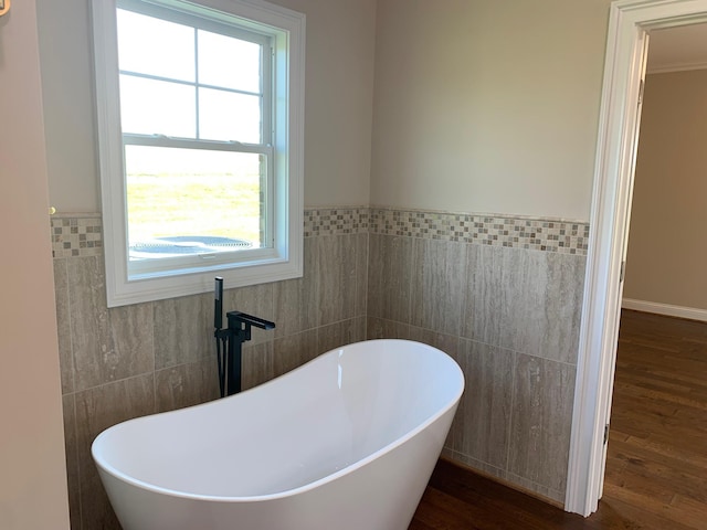 bathroom featuring a healthy amount of sunlight, a bathtub, tile walls, and hardwood / wood-style flooring