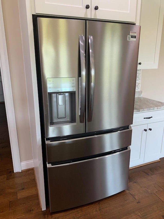 interior details with dark wood-type flooring, stainless steel fridge, and white cabinetry