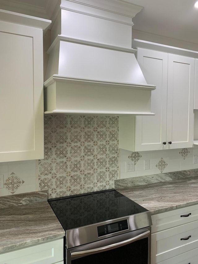 kitchen with electric range, light stone counters, crown molding, and white cabinetry