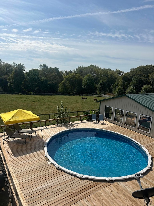 view of swimming pool with a deck, a lawn, and a rural view