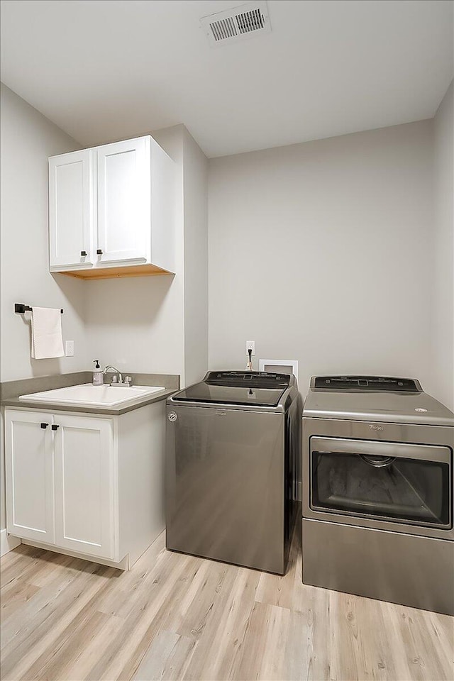 clothes washing area featuring cabinets, separate washer and dryer, sink, and light hardwood / wood-style flooring