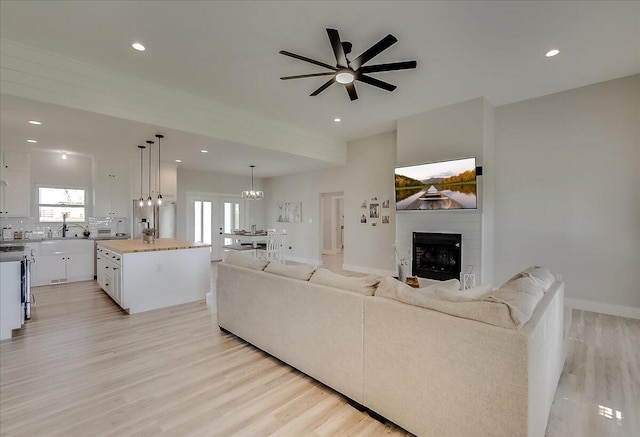 living room featuring a fireplace, light hardwood / wood-style floors, ceiling fan, and sink