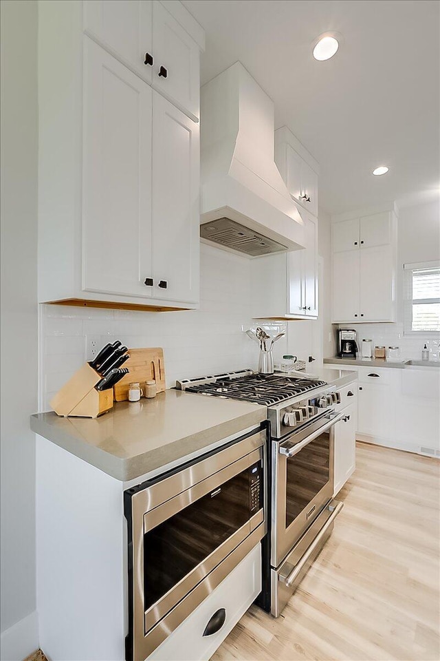 kitchen with white cabinetry, sink, stainless steel appliances, premium range hood, and light wood-type flooring