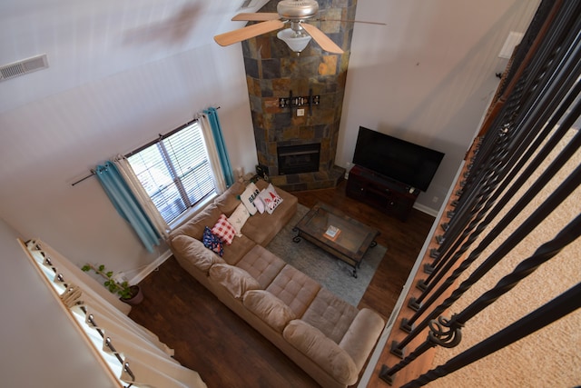 living room with a stone fireplace, ceiling fan, hardwood / wood-style floors, and a towering ceiling