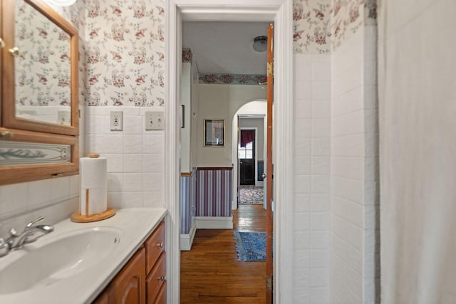 bathroom with vanity, wainscoting, wood finished floors, tile walls, and wallpapered walls