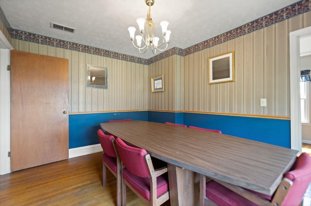 dining area with an inviting chandelier, visible vents, wood finished floors, baseboards, and wallpapered walls