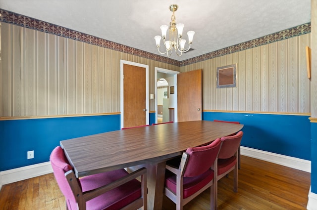 dining space with an inviting chandelier, baseboards, wood-type flooring, and wallpapered walls