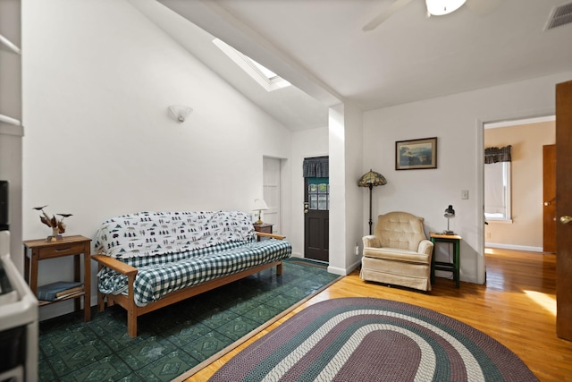 living area featuring ceiling fan, high vaulted ceiling, wood finished floors, a skylight, and visible vents
