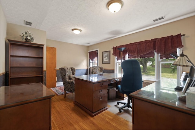 office area featuring light wood finished floors, a textured ceiling, and visible vents