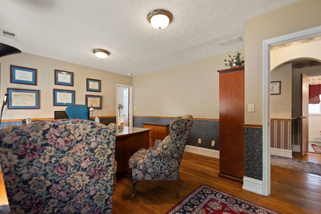 sitting room with a textured ceiling, visible vents, arched walkways, wainscoting, and wood finished floors