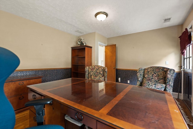 dining area with visible vents, a textured ceiling, and a wainscoted wall