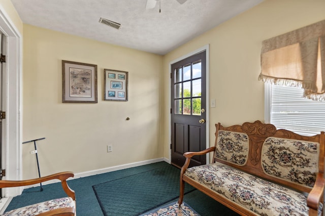 interior space featuring carpet floors, visible vents, baseboards, a textured ceiling, and a ceiling fan