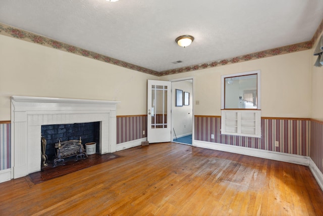 unfurnished living room with wood-type flooring, a brick fireplace, and a wainscoted wall