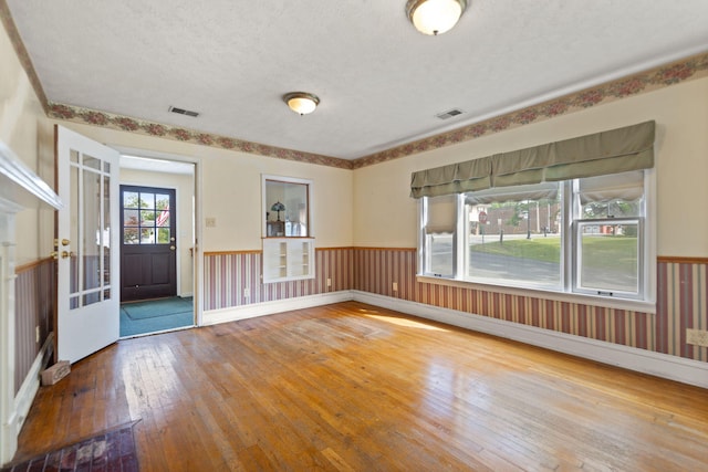 unfurnished room featuring a wainscoted wall, hardwood / wood-style flooring, a textured ceiling, and visible vents