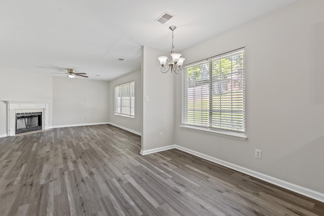 unfurnished living room with baseboards, visible vents, wood finished floors, a fireplace, and ceiling fan with notable chandelier