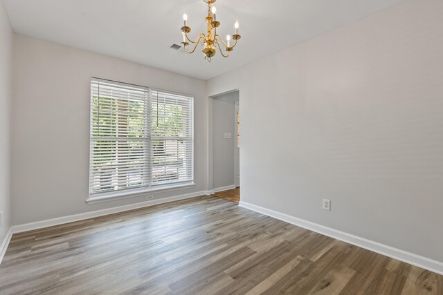 empty room featuring baseboards, wood finished floors, visible vents, and an inviting chandelier