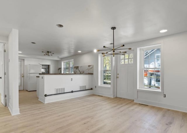 unfurnished living room featuring light wood-type flooring, a healthy amount of sunlight, and an inviting chandelier