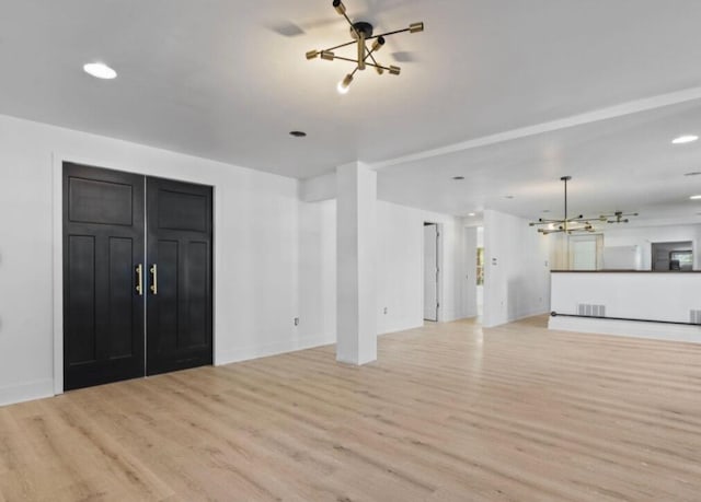 unfurnished living room featuring a notable chandelier and light hardwood / wood-style flooring