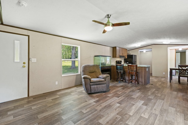 living room with a textured ceiling, ceiling fan, light hardwood / wood-style flooring, and vaulted ceiling