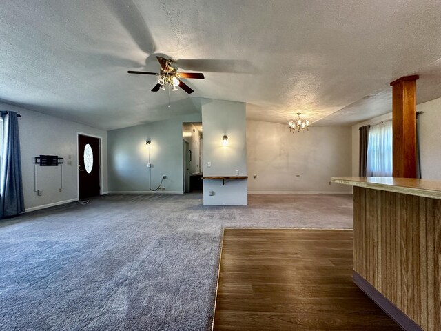 unfurnished living room featuring baseboards, lofted ceiling, a textured ceiling, carpet floors, and ceiling fan with notable chandelier