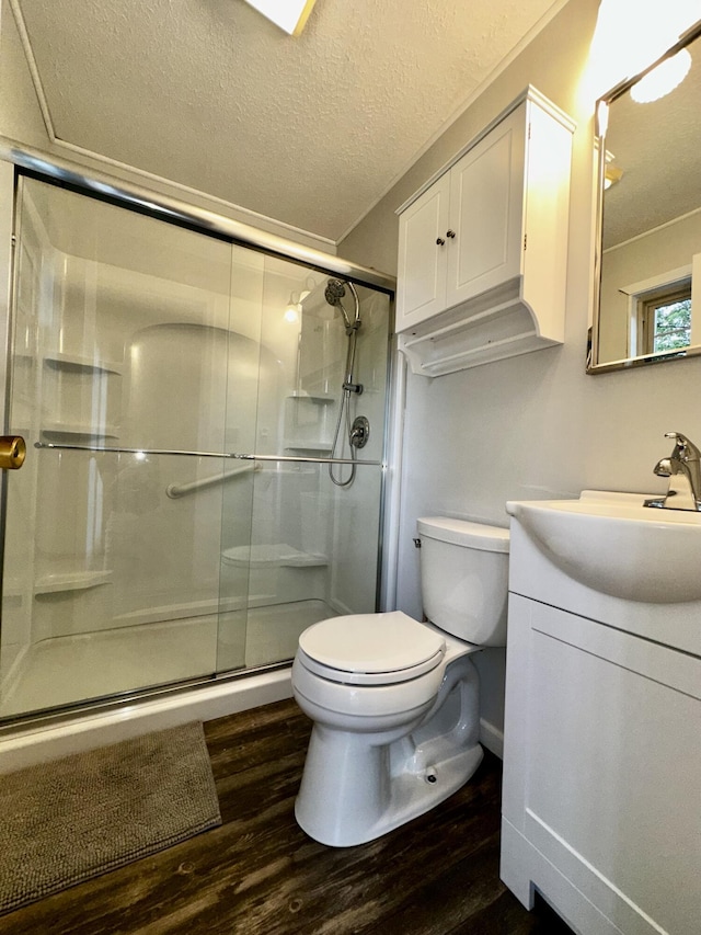 bathroom with a textured ceiling, a shower with shower door, toilet, wood finished floors, and vanity