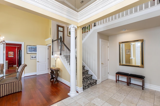 foyer entrance with ornate columns, a towering ceiling, ornamental molding, light hardwood / wood-style floors, and an inviting chandelier