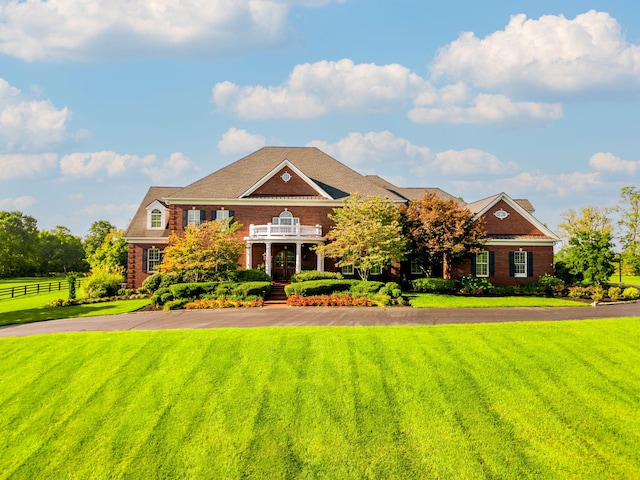 colonial-style house with a balcony, driveway, a front lawn, and fence