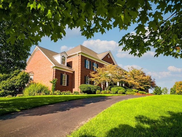 view of side of home featuring aphalt driveway, a yard, and brick siding