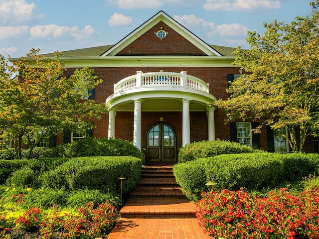 view of exterior entry featuring brick siding, french doors, and a balcony