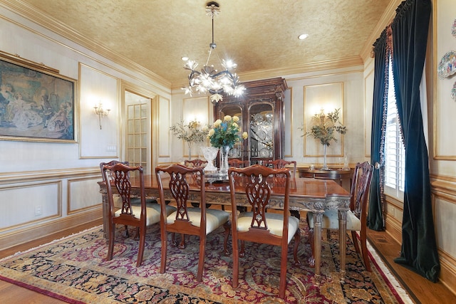 dining room with wood finished floors, a textured ceiling, crown molding, a decorative wall, and a notable chandelier