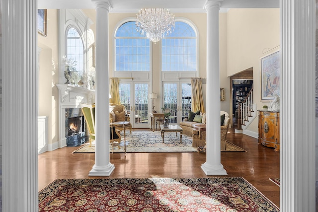 foyer entrance featuring wood finished floors, an inviting chandelier, a high ceiling, decorative columns, and a warm lit fireplace