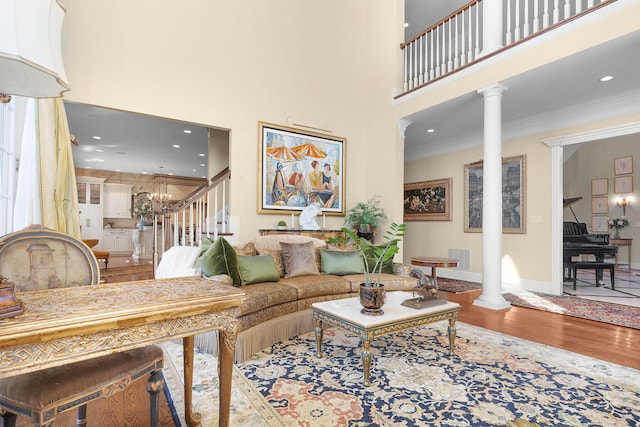 living area with a towering ceiling, crown molding, ornate columns, and wood finished floors