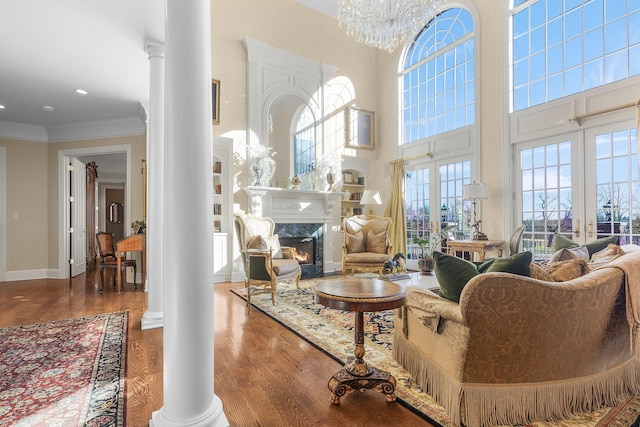 living area featuring ornamental molding, wood finished floors, a fireplace, decorative columns, and baseboards