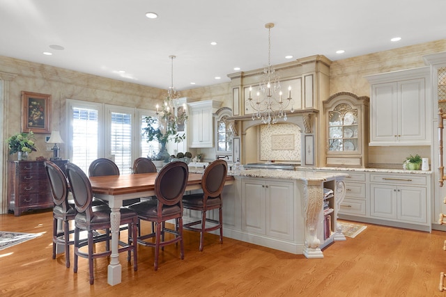 kitchen featuring light wood finished floors, a notable chandelier, hanging light fixtures, and light stone countertops