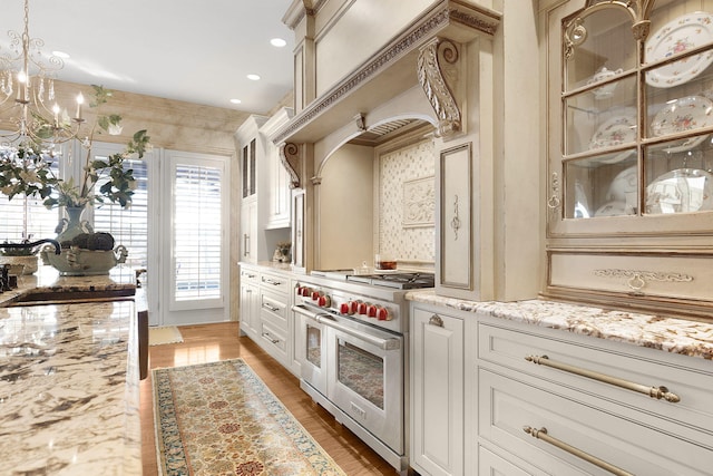 kitchen with light stone countertops, light wood finished floors, an inviting chandelier, range with two ovens, and a sink