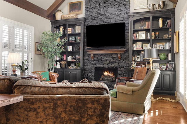 living room featuring a stone fireplace, vaulted ceiling with beams, and wood finished floors