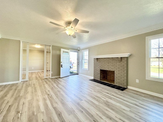 unfurnished living room featuring crown molding, light hardwood / wood-style flooring, a brick fireplace, a textured ceiling, and ceiling fan