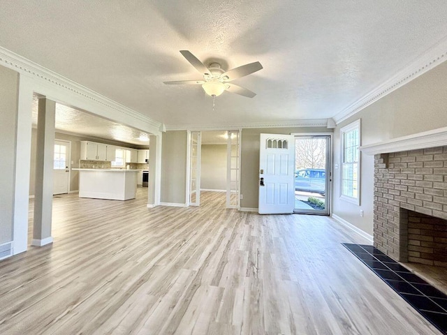 unfurnished living room with crown molding, a brick fireplace, a textured ceiling, ceiling fan, and light hardwood / wood-style floors