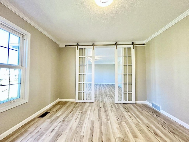 empty room with ornamental molding, a barn door, light hardwood / wood-style floors, and a textured ceiling