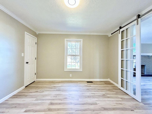 unfurnished room with ornamental molding, a barn door, a textured ceiling, and light wood-type flooring