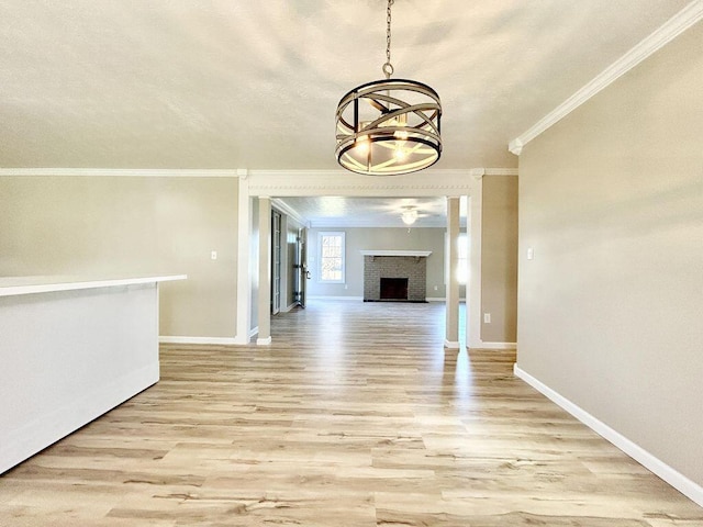 unfurnished dining area featuring crown molding, a fireplace, light hardwood / wood-style floors, and a notable chandelier