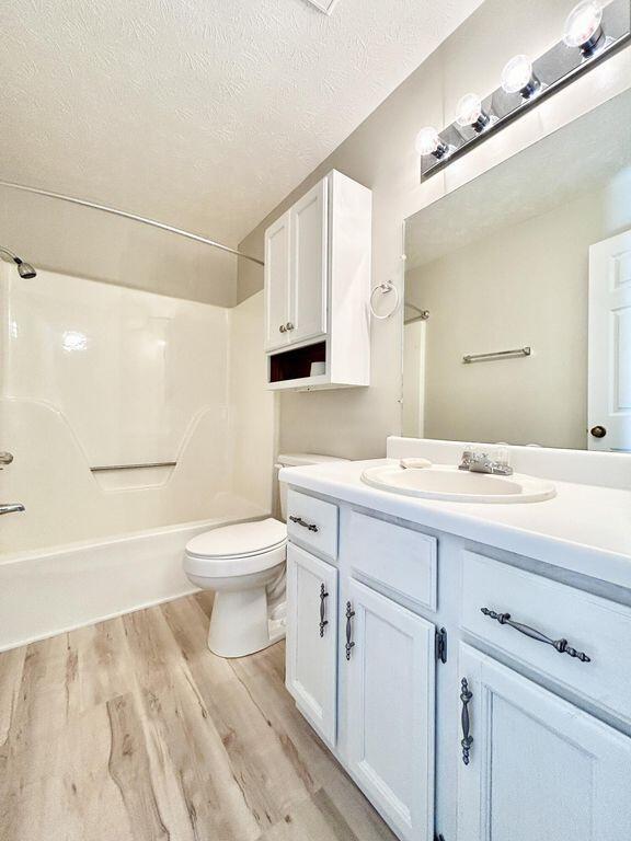 full bathroom featuring toilet, a textured ceiling, shower / tub combination, vanity, and hardwood / wood-style floors