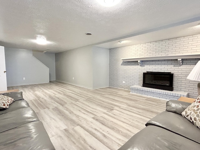 living room featuring brick wall, a brick fireplace, light hardwood / wood-style floors, and a textured ceiling