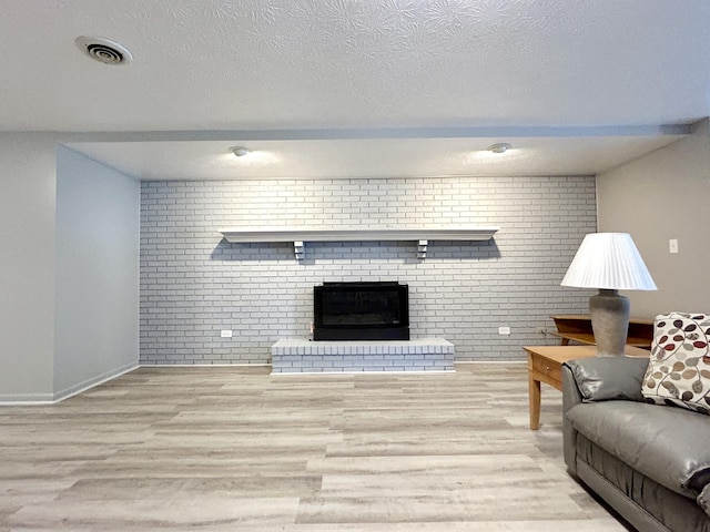 living room featuring brick wall, a textured ceiling, light hardwood / wood-style floors, and a brick fireplace