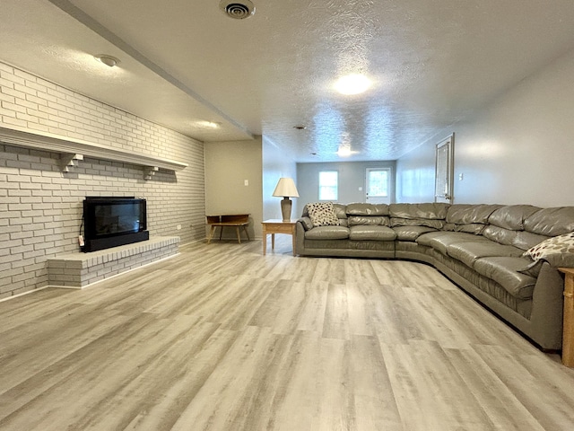 unfurnished living room featuring brick wall, a brick fireplace, a textured ceiling, and light hardwood / wood-style flooring