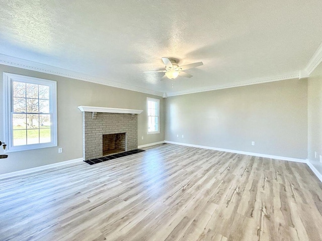 unfurnished living room with ornamental molding, a brick fireplace, a textured ceiling, and light wood-type flooring