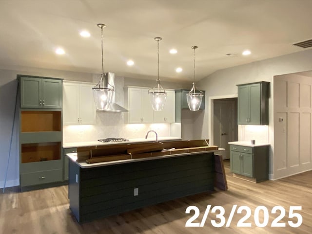 kitchen with a kitchen island with sink, white cabinetry, wall chimney exhaust hood, decorative light fixtures, and stainless steel gas stovetop